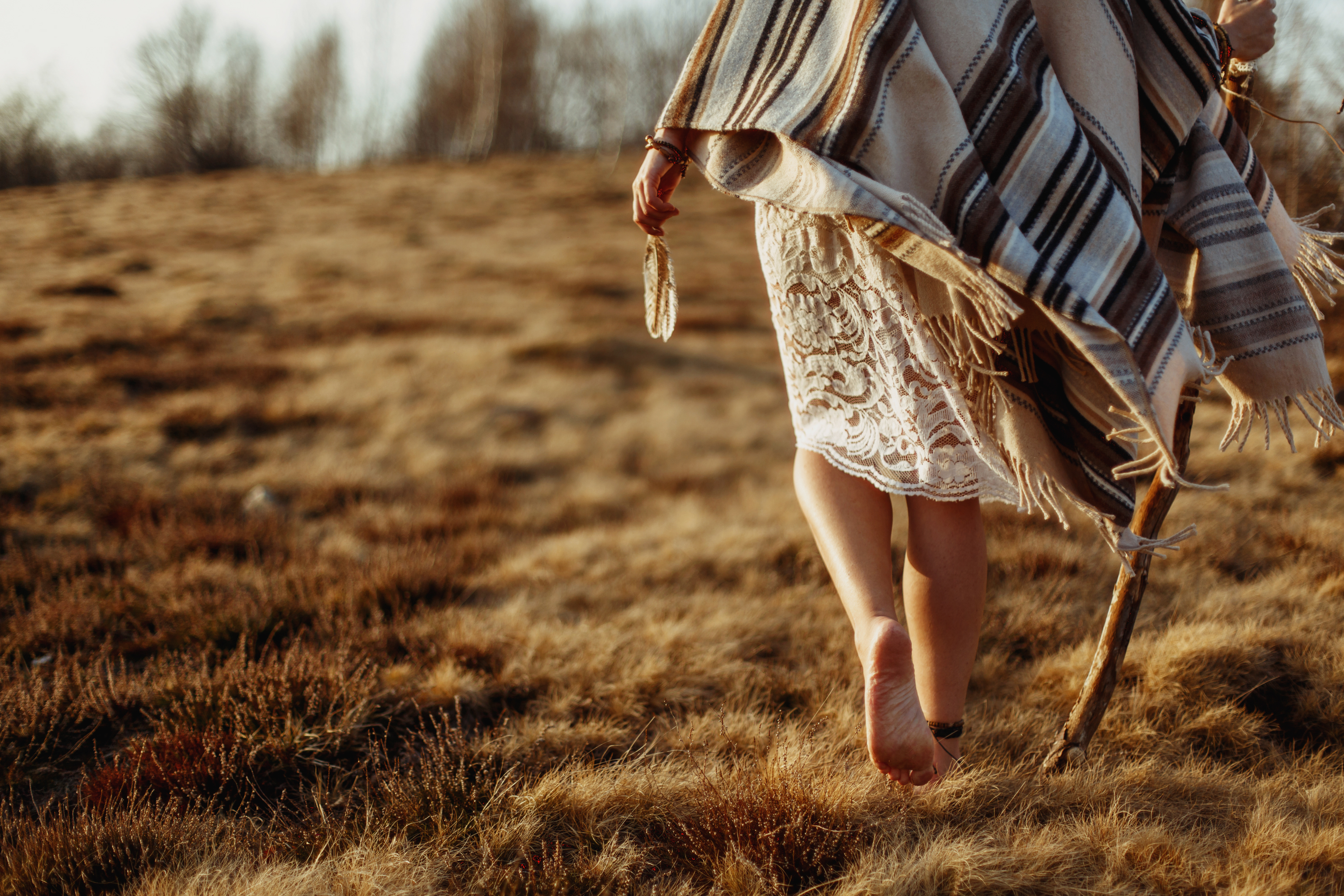 woman legs in native indian american boho dress walking in windy sunny evening mountains, holding feathers